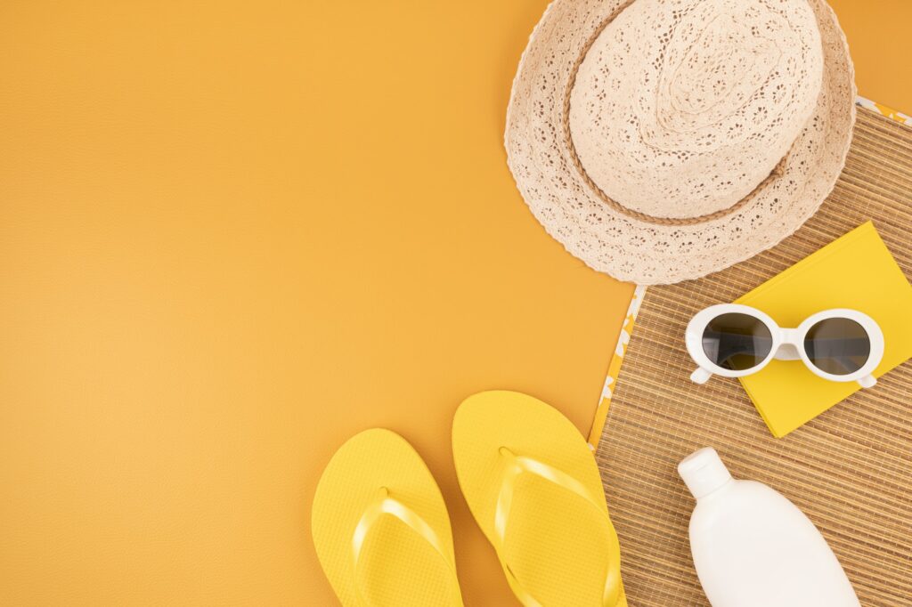 Flat lay with summer accessories for woman. Sun hat, sunglasses, sunscreen protection, flip flops